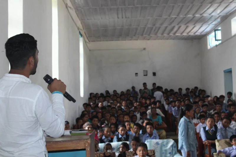 Dheeraj Joshi with a microphone addressing a hall full of schoolchildren.