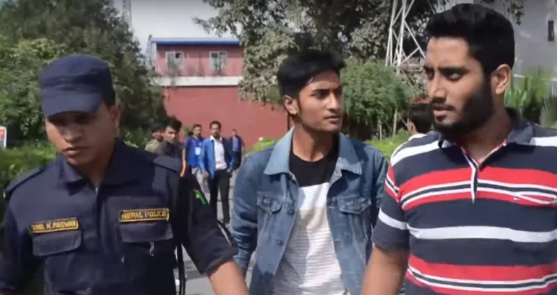 A police officer walking beside Dheeraj Joshi, in a striped shirt, and another young man.