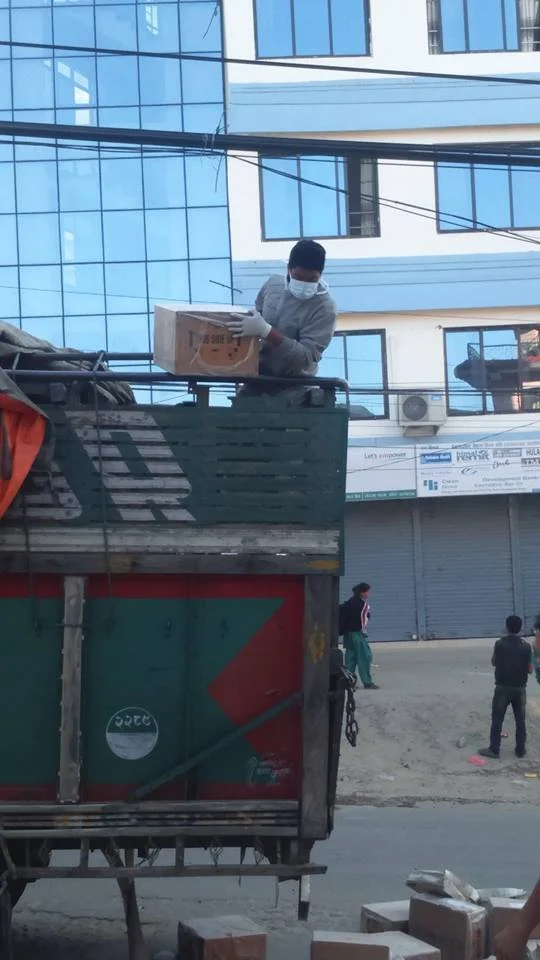 A volunteer in a face mask lifting boxes on top of a truck.