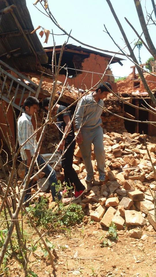 Volunteers walking across the rubble of a collapsed brick house.