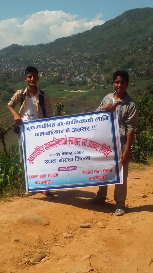 Two young volunteers on a hillside holding a banner for a children’s care camp in Gorkha district.