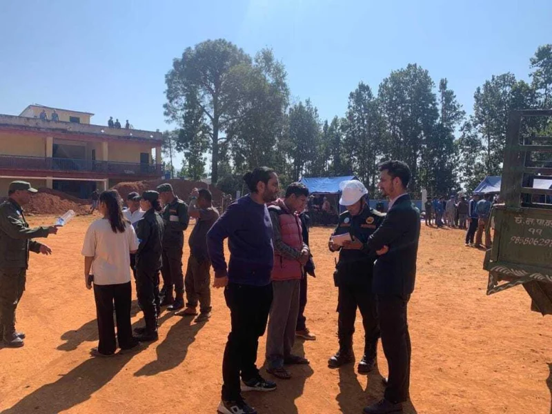 Officials and volunteers gathered on an open ground near a building and parked trucks.