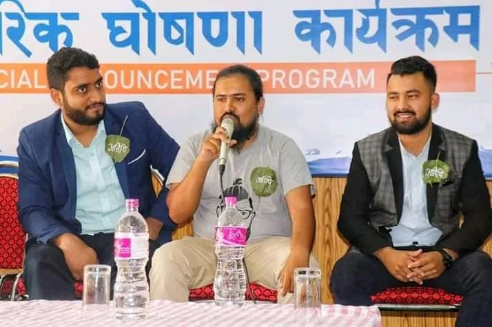 Three men seated on a panel, the centre speaker holding a microphone.