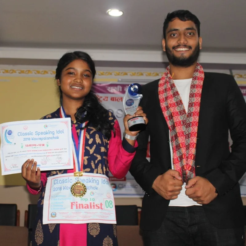 A smiling student holding a certificate and trophy stands beside Dheeraj Joshi.